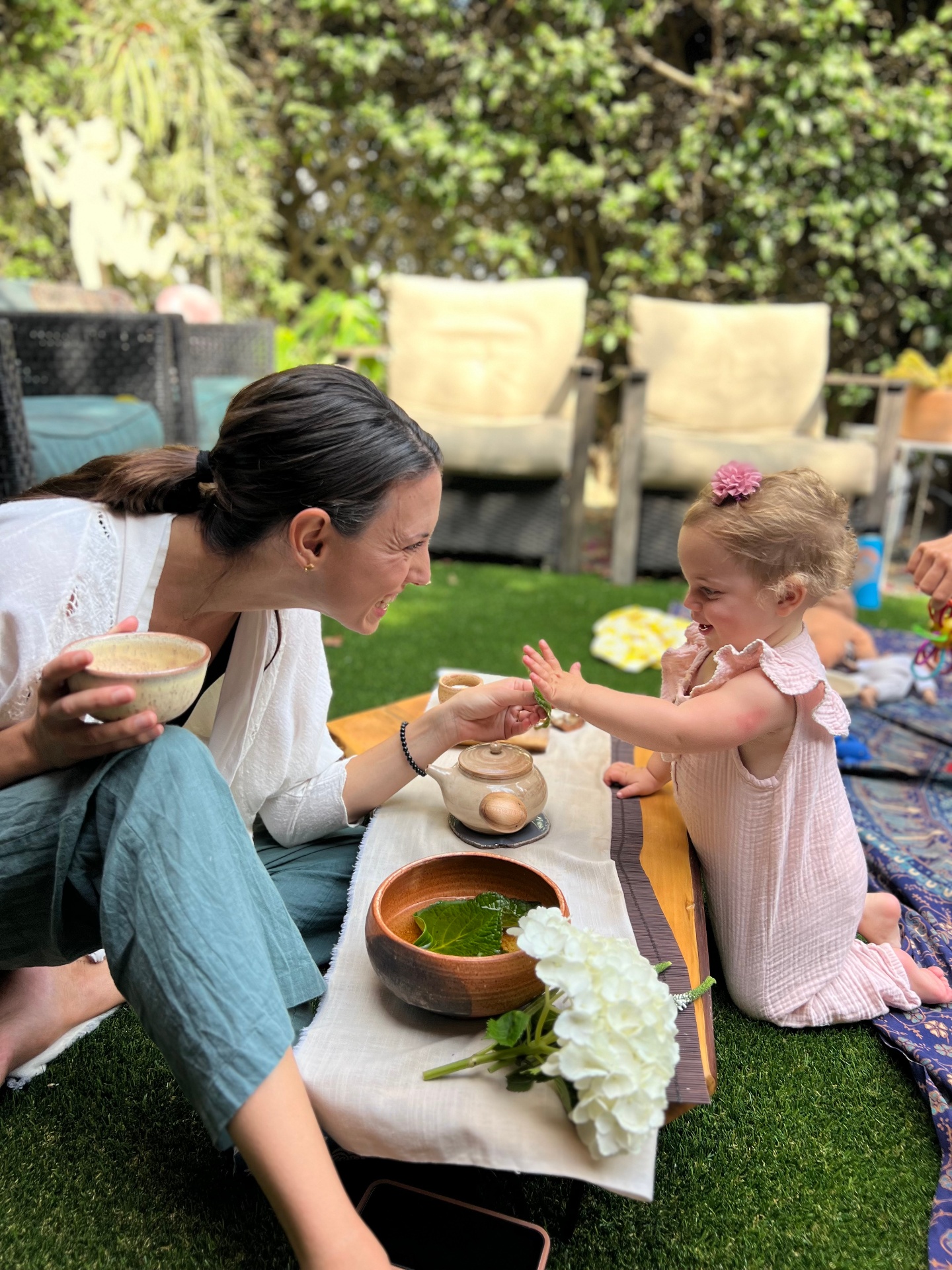 An occupational therapist sharing a joyful garden tea party moment with a smiling toddler during an in-home pediatric OT session