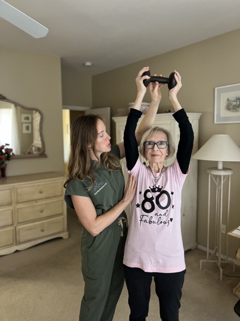 An occupational therapist guiding an older woman through a strength exercise at home