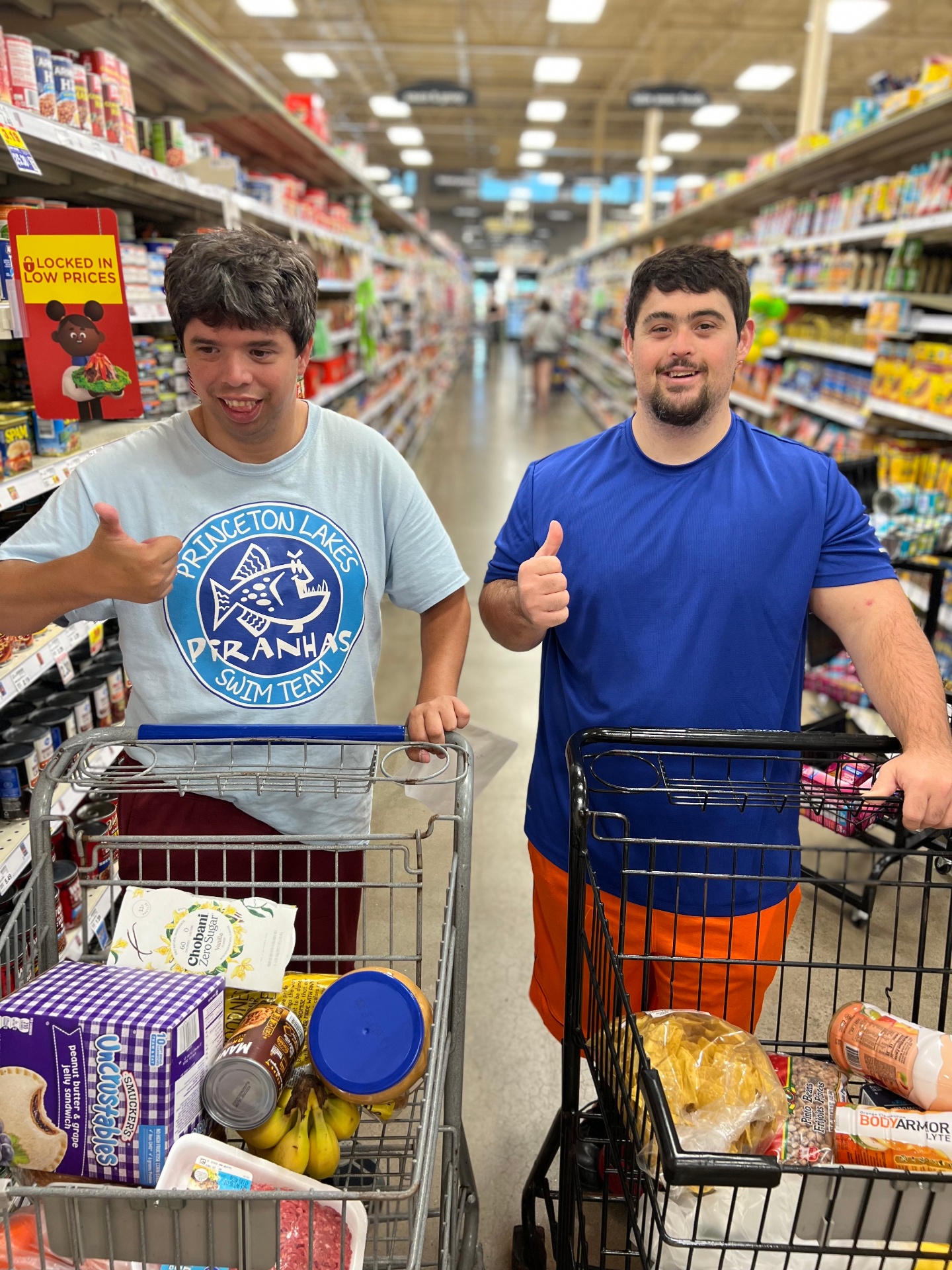 Two young adults giving a thumbs up while grocery shopping together, building real-world independent living skills