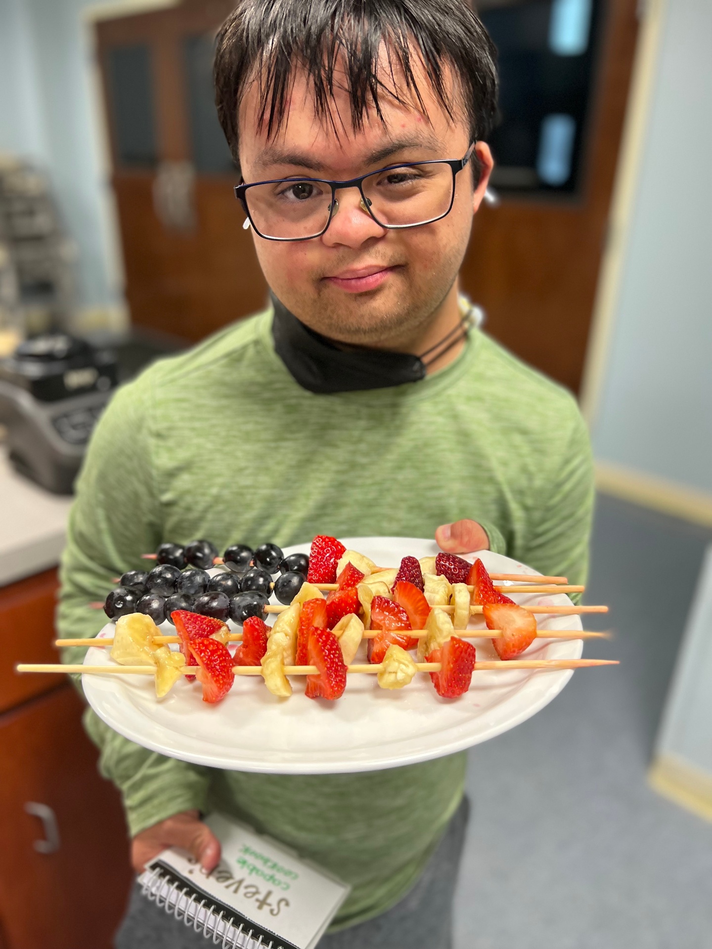 Young adult proudly displaying fruit skewers he prepared